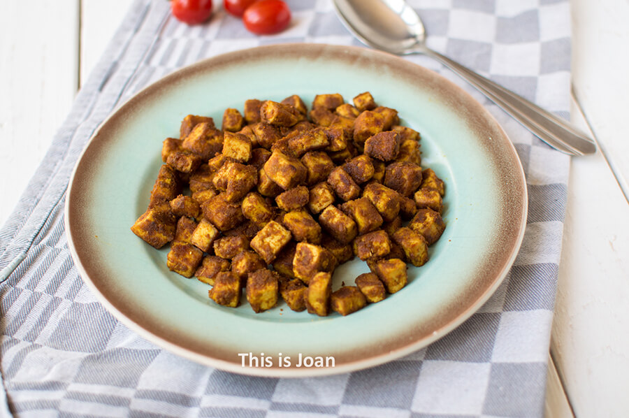 een geruite theedoek met daarop een turquoise bord met stukjes vegan gemarineerde tofu op Indonesische wijze