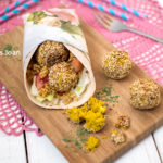 een roze kleedje met daarop een snijdplank met een wrap en vier balletjes glutenvrije falafel