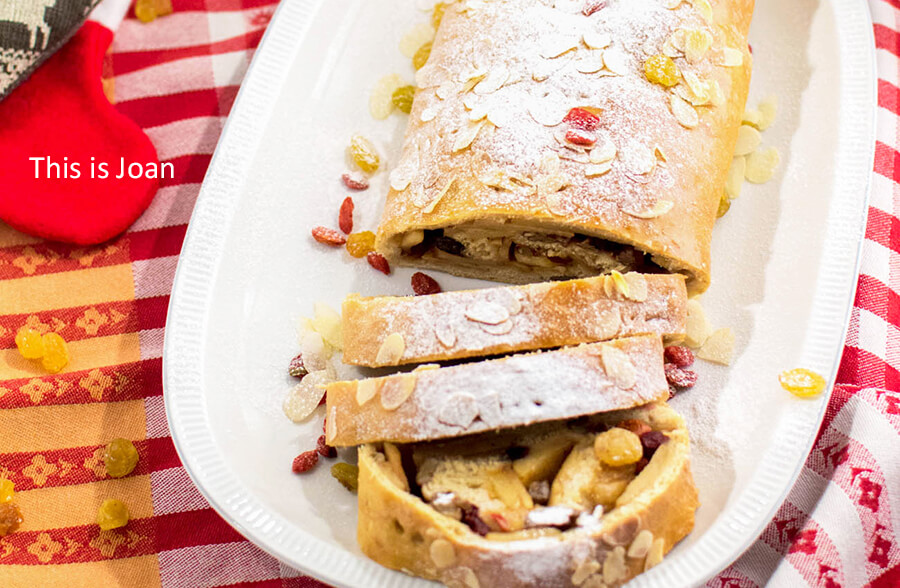 een rood tafelkleed met daarop een wit ovalen bord met een vegan apfelstrudel die is gegarneerd met gele rozijnen, poedersuiker en goij bessen