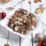 een wit, vierkant bakje met daarin glutenvrije kerstkransjes die zijn gegarneerd met pure chocolade en amandelschaafsel