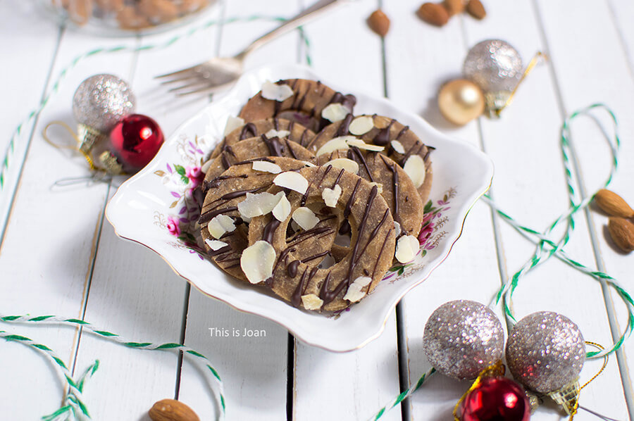 een wit, vierkant bakje met daarin glutenvrije kerstkransjes die zijn gegarneerd met pure chocolade en amandelschaafsel