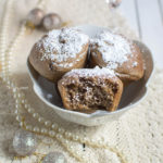 een beige kleed met daarop een witte kom met daarin 3 oliebollen uit de oven die zijn bestrooid met poedersuiker