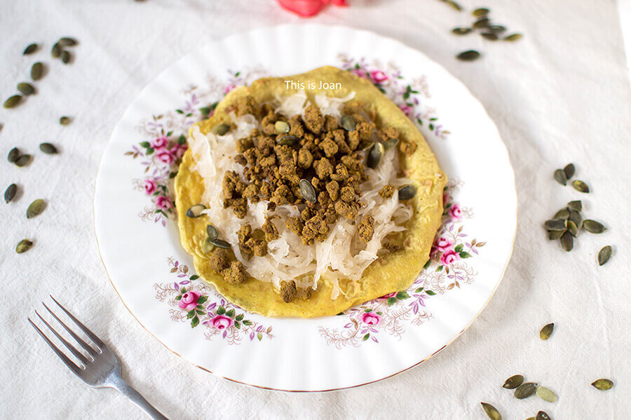 wit bord met roze bloemen met daarop een zuurkoolwrap met vegan gehakt en pompoempitten