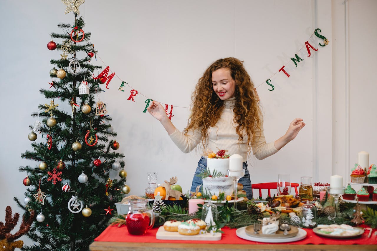 een blije jonge vrouw kijkt trots dat ze een vegan kerstontbijt heeft samengesteld met taart en ander kersteten